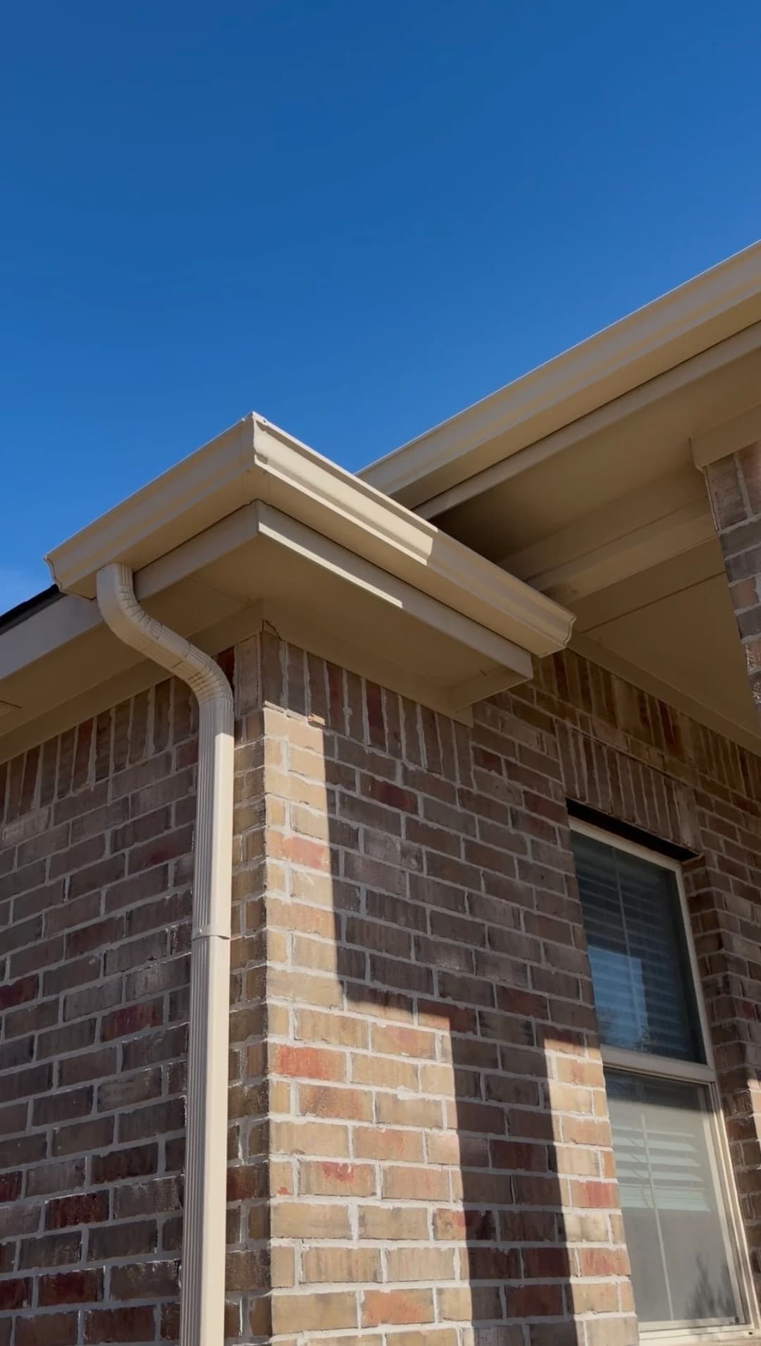 Residential brick home corner with guttering against a clear blue sky.