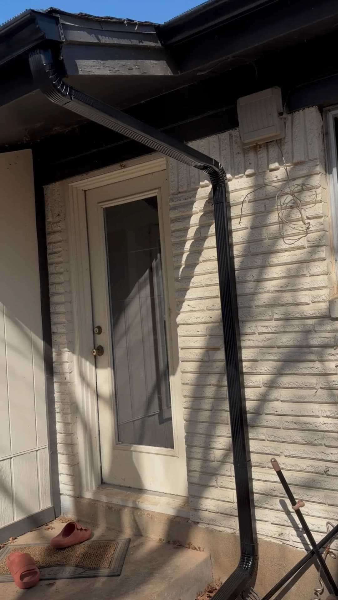 Black rain gutter system along a house exterior, directing water away from the entryway.