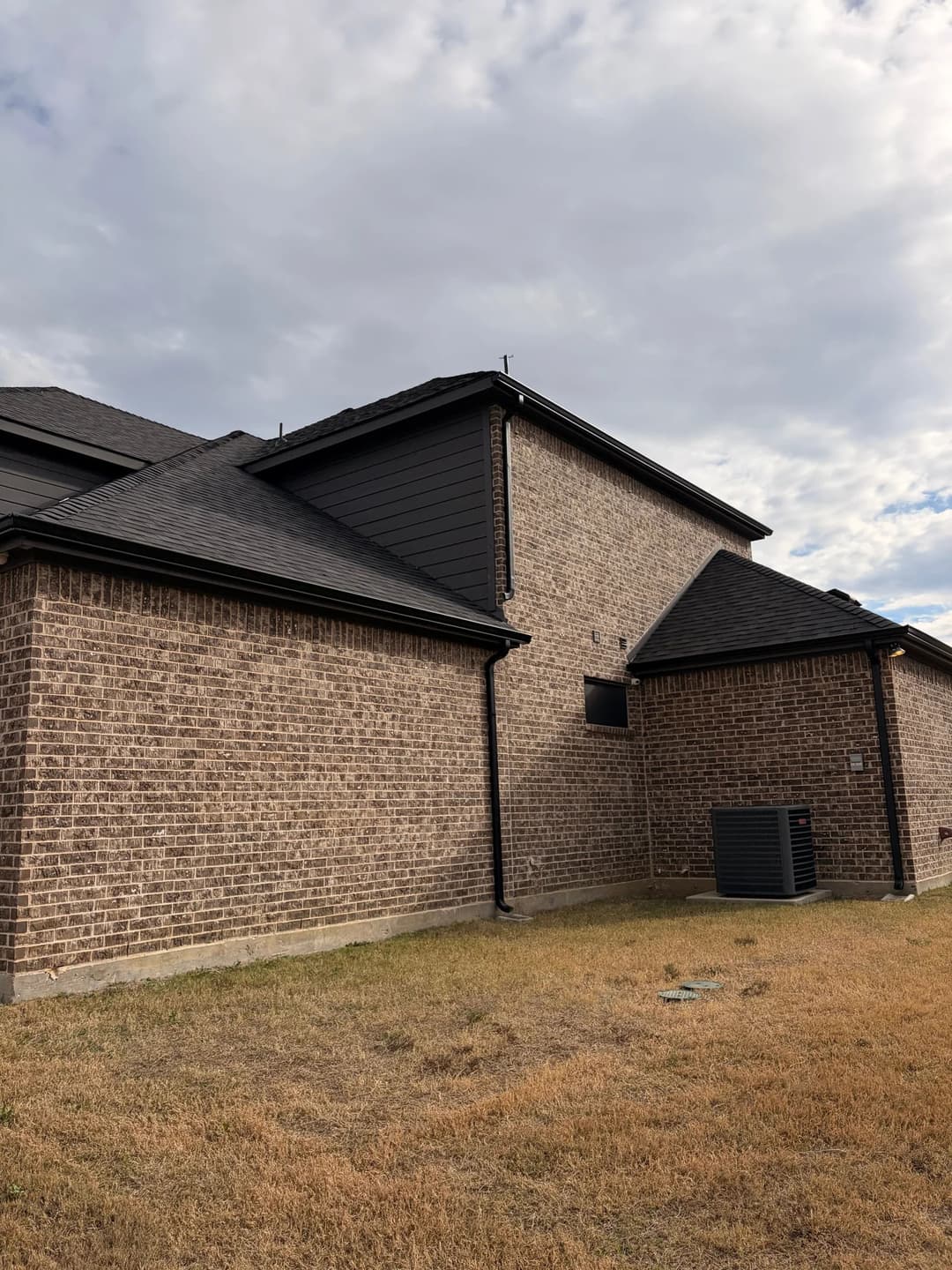 Modern brick house exterior with black siding and air conditioning unit on grassy yard.
