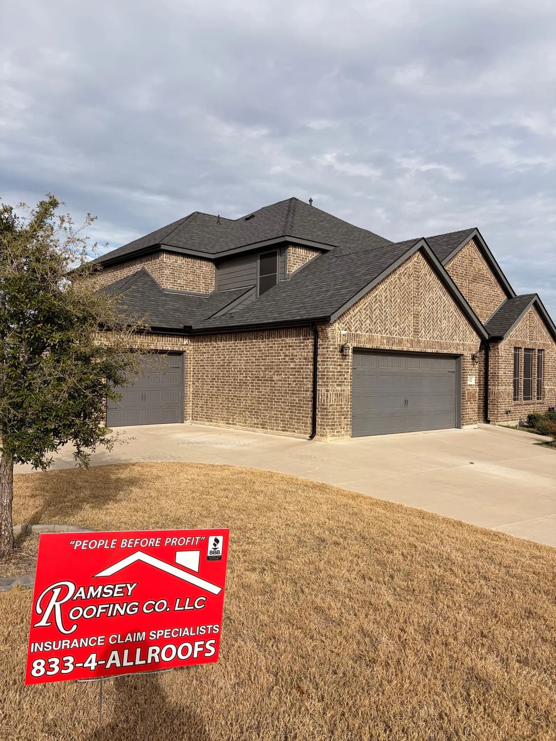 Newly constructed brick home with dark roof, featuring a sign for Ramsey Roofing Co. insurance claims.