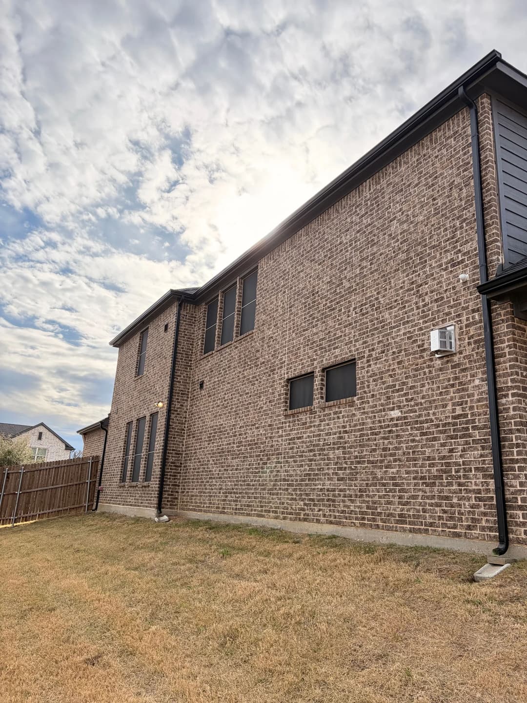 Modern two-story brick home exterior with large windows and cloudy sky backdrop.