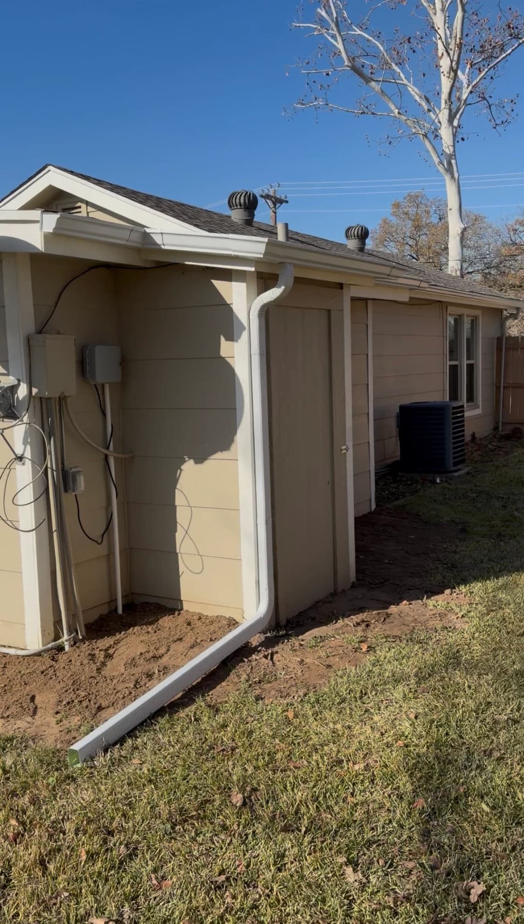 Side view of a house featuring a shed, downspout, and HVAC unit on a sunny day.