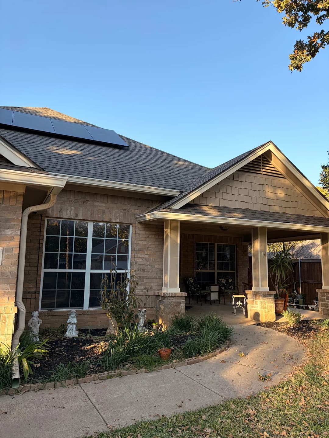 Brick home with solar panels, lush greenery, and a welcoming porch under a clear blue sky.