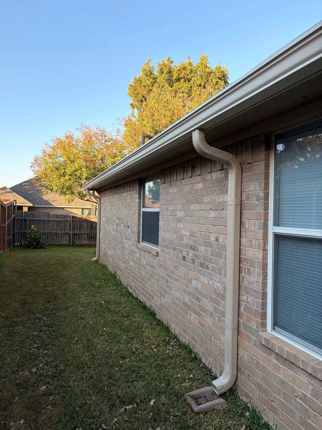 Side view of a brick house showing drainage pipe and well-maintained lawn.