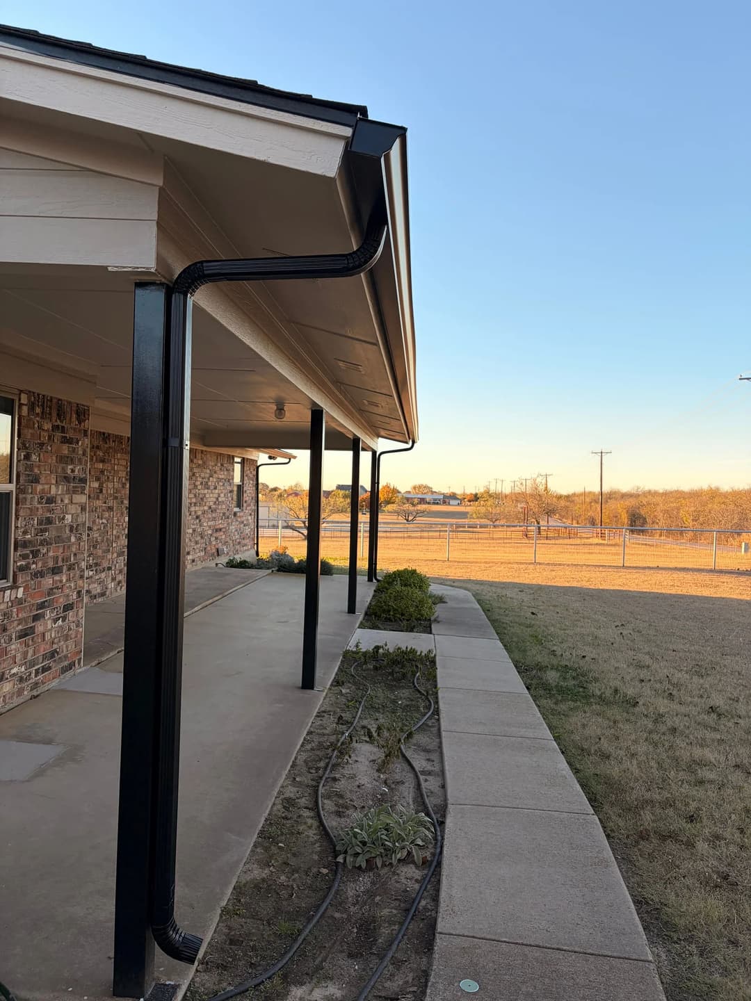 Modern home exterior featuring black metal gutters, concrete walkway, and landscaped garden.