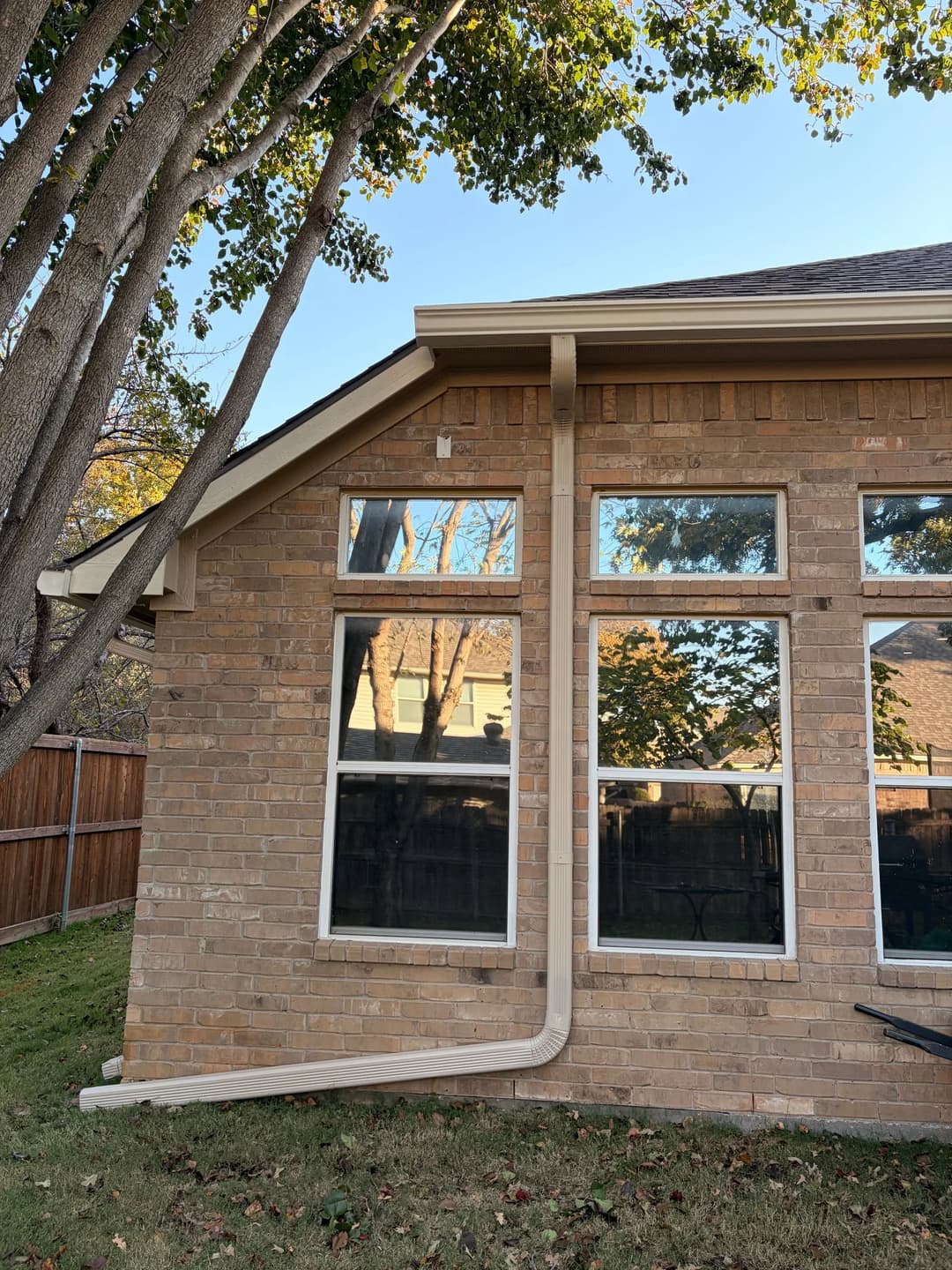 Brick house exterior with large windows and a neatly installed downspout in a residential area.