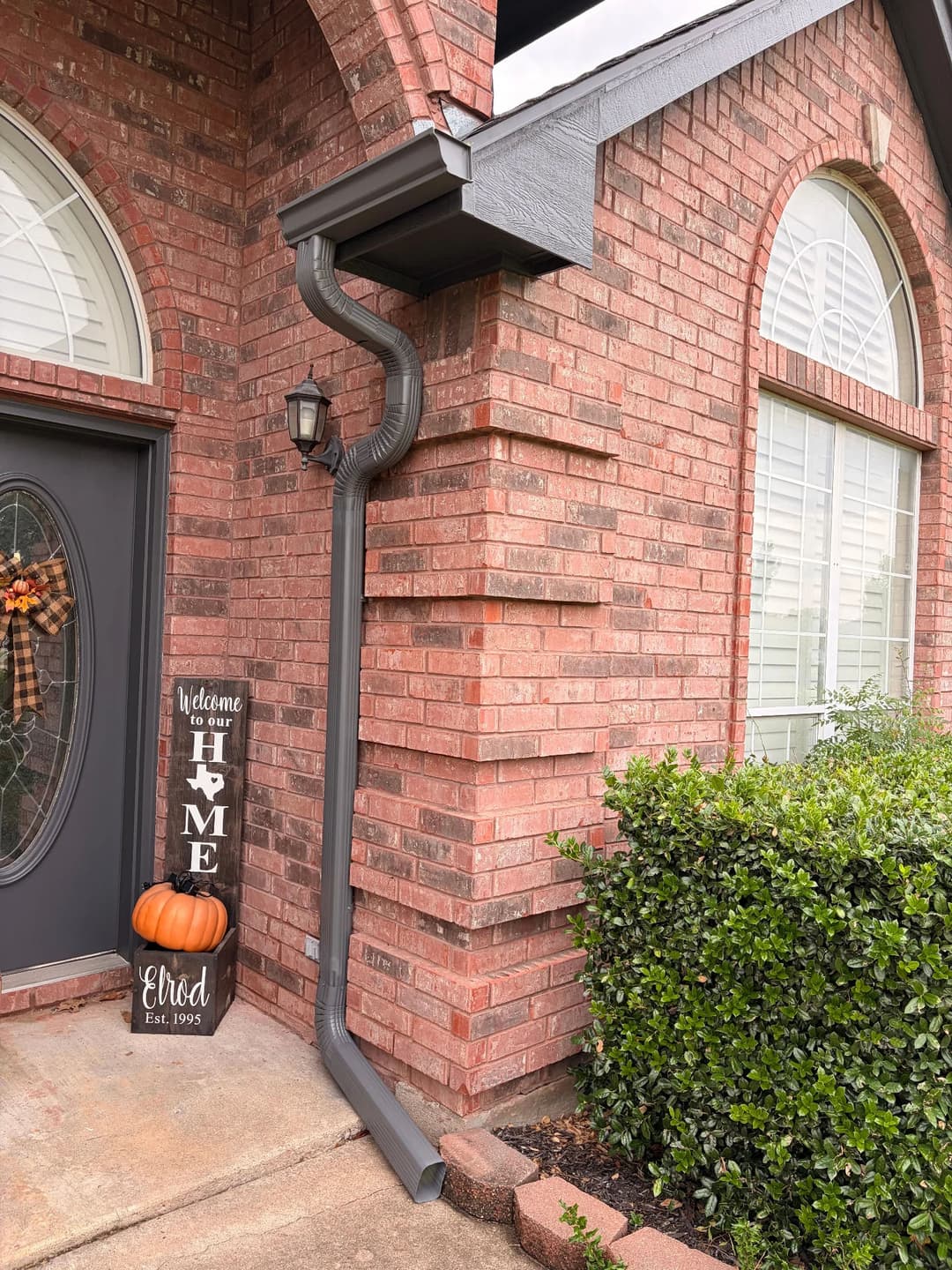 Brick home entrance with rain gutter, decorative sign, pumpkin, and greenery.
