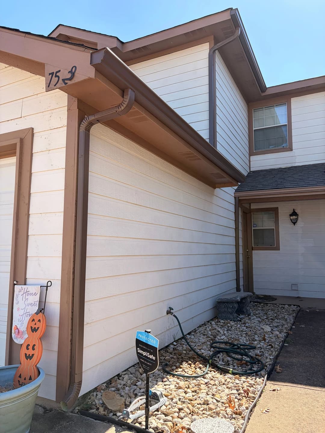 Corner of a residential home with beige siding, brown trim, and decorative garden elements.