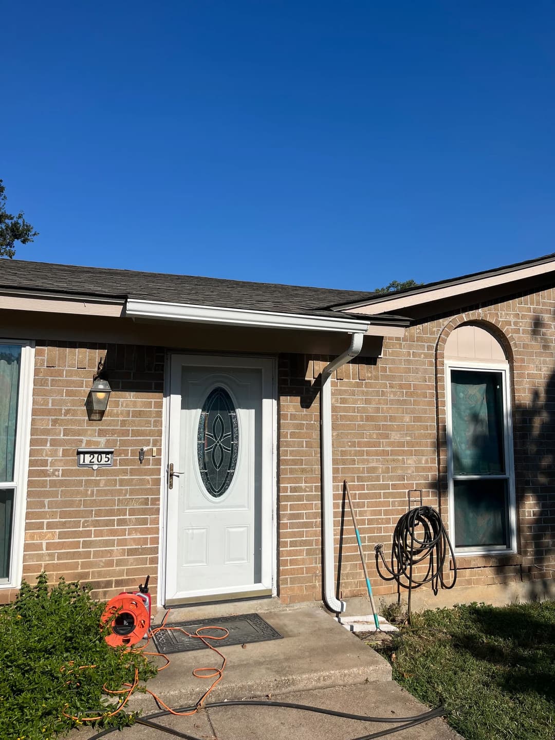Front view of a brick house with a white door, clear sky, and lawn maintenance equipment.